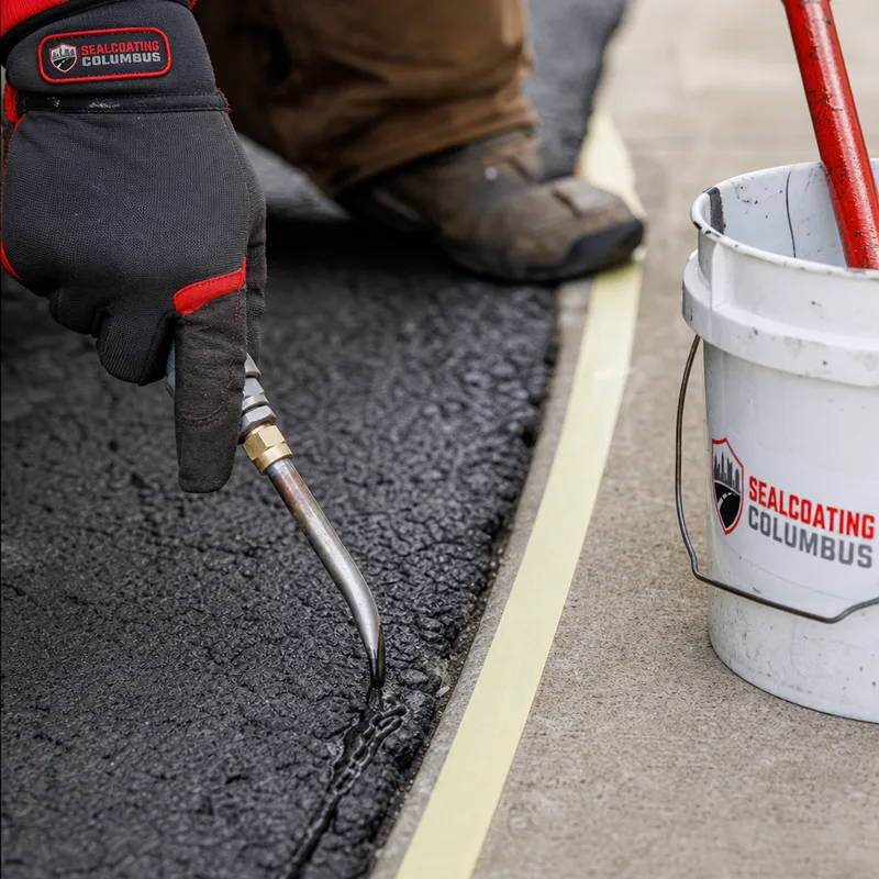 Cleaned asphalt driveway with a prepared crack and masked edge beside a concrete sidewalk